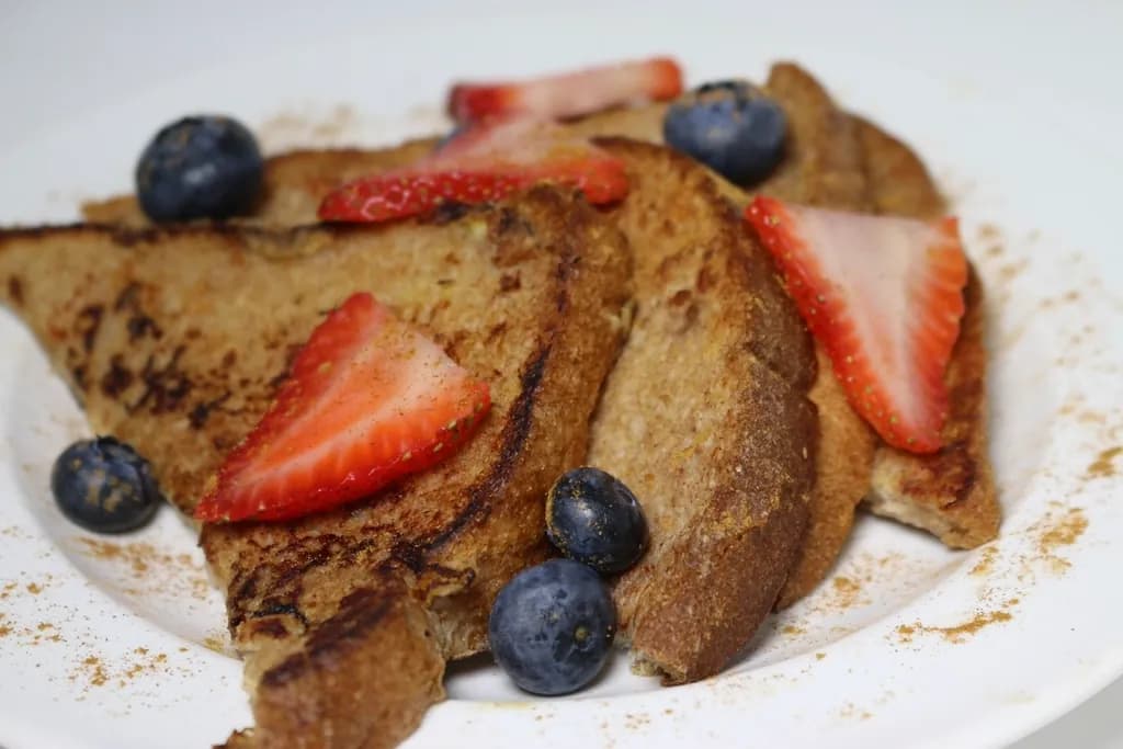 Tostadas francesas: Pan brioche bañado en huevo y canela, dorado en mantequilla, con fresas, arándan