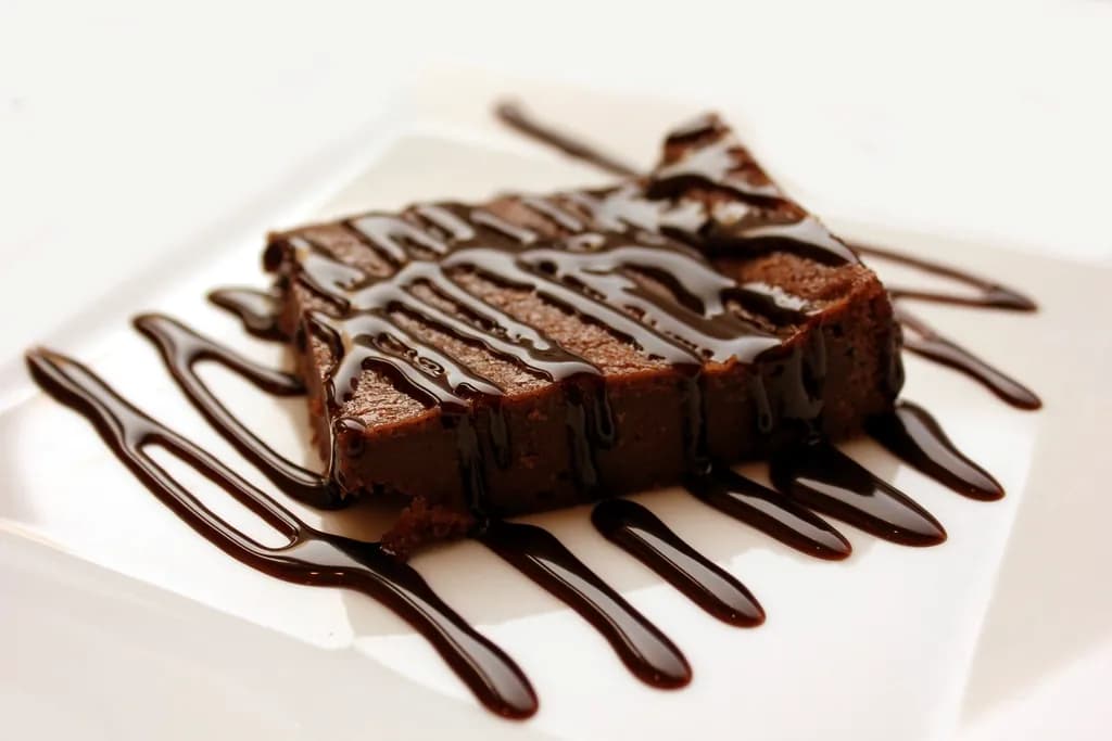 Brownie de chocolate: Brownie denso y melcochudo, con costra brillante y bañado en salsa de chocolate.